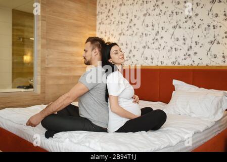 Moglie incinta e marito seduto in posa yoga Foto Stock