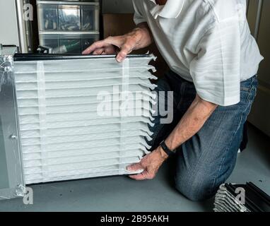 Uomo caucasico senior che controlla un filtro dell'aria piegato pulito nel sistema del forno HVAC nel seminterrato della casa Foto Stock