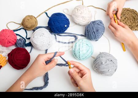 Palle di filato di colore diverso. Le mani dei bambini sono accovacciate e la vista del filo da sopra sul tavolo bianco Foto Stock