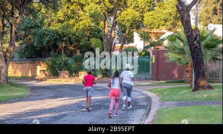 Alberton, Sud Africa - madre non identificata e i suoi due bambini jogging in un'immagine di strada residenziale in formato orizzontale Foto Stock
