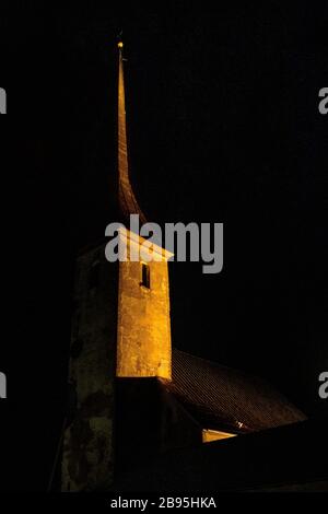 Vista della torre della chiesa di notte. Torre illuminata con orologio su sfondo scuro.Foto notturna dell'imponente Castello, torre. Chiesa antica Foto Stock