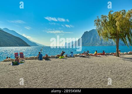 Torbole, Italia-09 Ottobre 2018: Persone sedute in spiaggia sulla poltrona e ammirando il Lago di Garda in estate, vista sul bellissimo Lago Foto Stock