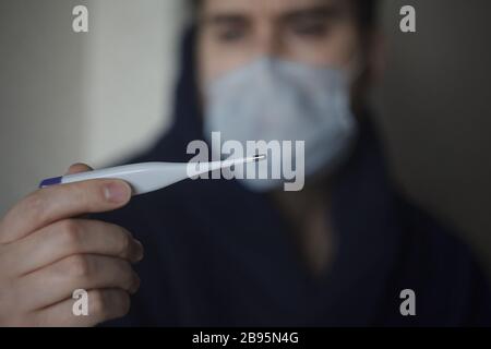 L'uomo offuscato nella maschera di medicina tenendo il termometro davanti a lui Foto Stock