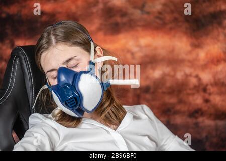 Donna in una maschera a gas che dorme su una sedia. Coronovirus quarantena, soggiorno a casa, lavoro da casa concetto. Covid-19 pandemia Foto Stock