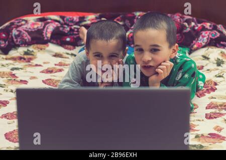 i fratelli wo in pigiama stanno guardando un cartone animato su un computer portatile. Bambini divertenti che godono di cartoni animati su notebook, laptop o computer. Foto Stock