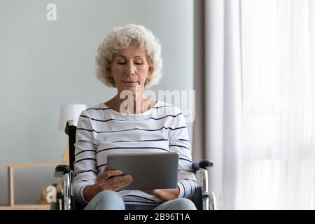 Donna anziana e intelligente disabilitata che naviga sul web su tablet Foto Stock
