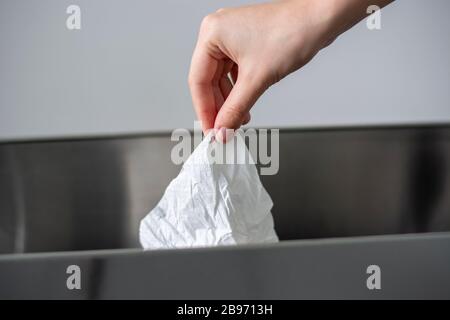 Le donne mano che getta una carta di tessuto sminuzzata bianca usata in un cestino di spazzatura. Concetto di igiene e cura della salute Foto Stock