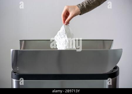 Le donne mano che getta una carta di tessuto sminuzzata bianca usata in un cestino di spazzatura. Concetto di igiene e cura della salute Foto Stock