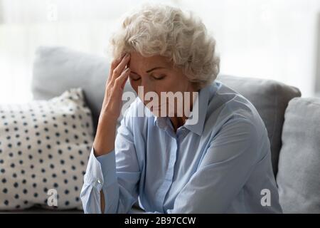 Donna anziana ammalata toccare la testa soffrendo di capogiri a casa Foto Stock