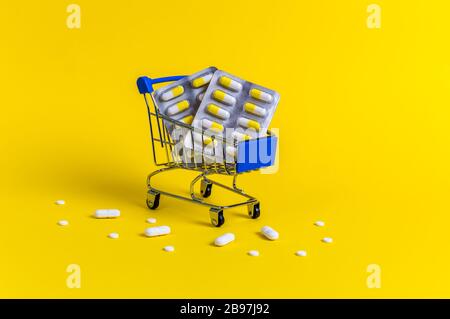 Carrello blu con blister e circondato da pillole bianche su sfondo giallo. Concetto creativo di sanità e shopping sicuro on-line per Foto Stock