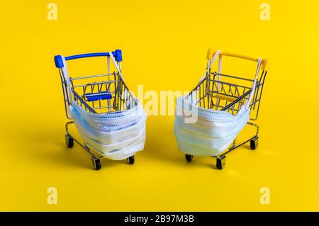 Due carrelli con maschere mediche per la protezione antivirus su sfondo giallo. Concetto creativo di sanità e shopping sicuro on-line su coronaviru Foto Stock