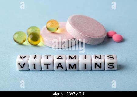 Le vitamine di parola fatte dei cubi bianchi e delle vitamine differenti su un fondo medico blu. Per ammalarsi, prendere pillole, sottoporsi al trattamento concetto. Assistenza sanitaria Foto Stock