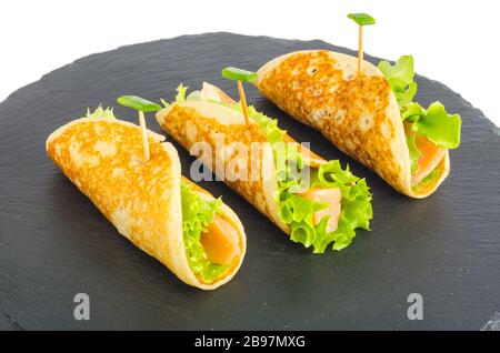 Involtini di pancake con pesce e lattuga. Pane al salmone con formaggio. Sulla piastra di pietra nera. Foto studio Foto Stock