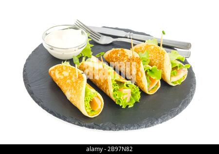 Involtini di pancake con pesce e lattuga. Pane al salmone con formaggio. Sulla piastra di pietra nera. Foto studio Foto Stock