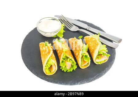 Involtini di pancake con pesce e lattuga. Pane al salmone con formaggio. Sulla piastra di pietra nera. Foto studio Foto Stock