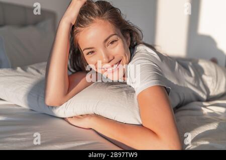 Bella donna asiatica che si rilassa a casa sul letto a cuscino in camera da letto e sorridente ritratto. Bellezza naturale modello sano della pelle faccia Foto Stock