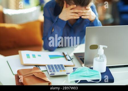 Primo piano su maschera medica e disinfettante per le mani e donna stressata in background in ufficio temporaneo durante l'epidemia di coronavirus in casa i Foto Stock