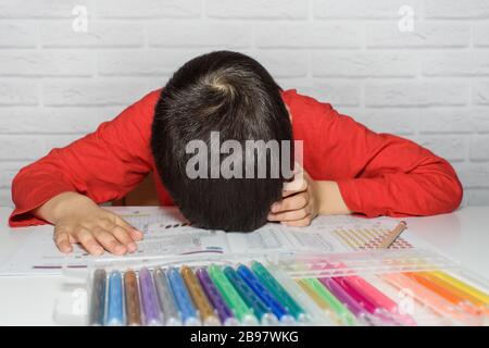 Sconvolto scolaro noioso facendo i compiti. Concetto di istruzione, scuola, difficoltà di apprendimento. Bambino stanco di fare i compiti studiando con la penna addormentata su OPE Foto Stock