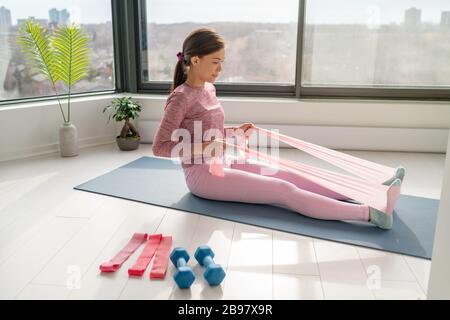 Allenamento domestico con banda di resistenza fitness Asian donna allenamento indietro muscoli con movimento del braccio che rotola usando le fasce di gomma sullo yoga esercizi di mat floor Foto Stock