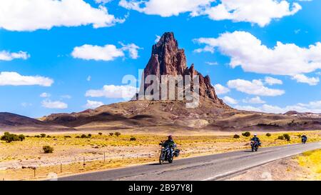 Tour in bici Riders passando le aspre vette di El Capitan e Agathla Peak torreggiando sul paesaggio desertico a sud della Monument Valley sulla US 163 Foto Stock