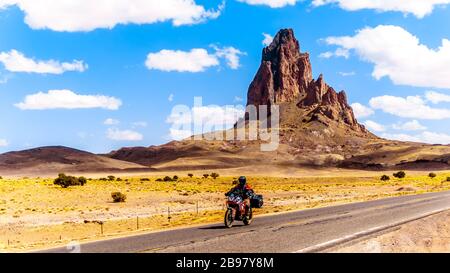 Tour in bici Riders passando le aspre vette di El Capitan e Agathla Peak torreggiando sul paesaggio desertico a sud della Monument Valley sulla US 163 Foto Stock