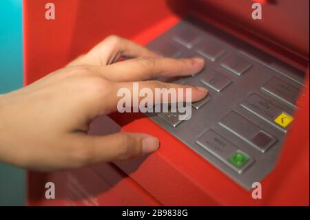 Donna mani per premere il tasto ATM nel cabinet rosso. Dito che preme un codice pin su un tastierino numerico. Codice di sicurezza su una macchina di teller automatica rossa ( Foto Stock