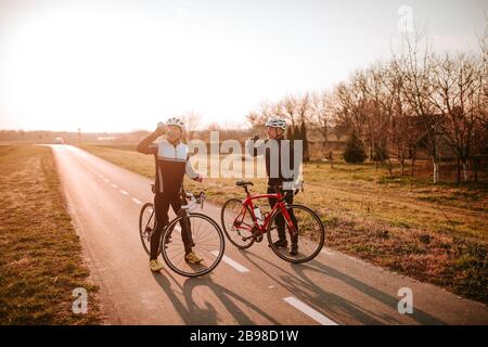 Due ciclisti di mezza età bevono acqua sulla strada. Riposo Foto Stock