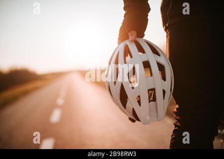 Il ciclista tiene il casco in mano e si alza sulla strada Foto Stock