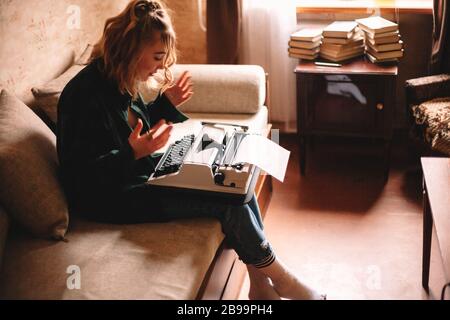 Giovane donna che cerca di utilizzare la macchina da scrivere mentre si siede sul divano a casa Foto Stock