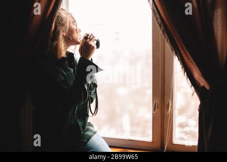 Giovane donna che scatta foto attraverso la finestra mentre si siede sul davanzale a casa Foto Stock