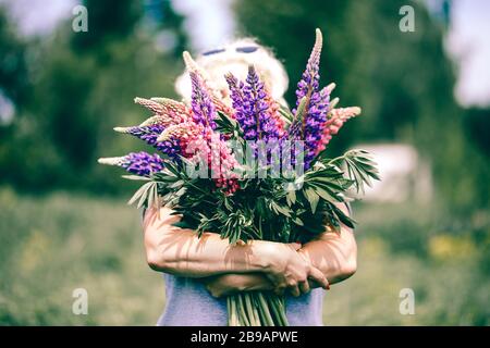 Donna bionda stout matura che tiene un bouquet lupino sullo sfondo della natura. Il concetto di bellezza e corpo positivo. Luce del tramonto Foto Stock