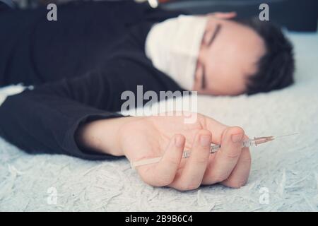 Un giovane è sdraiato sul pavimento con una siringa in mano, un sovradosaggio di farmaci. Il paziente con un'iniezione Foto Stock