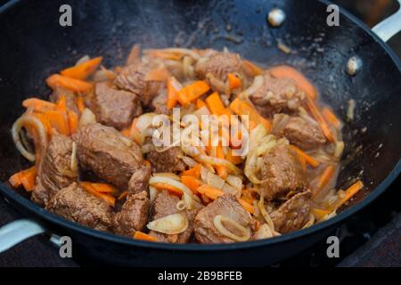 Pezzi di carne con carote e cipolle vengono stufati in un cavoldro al fuoco Foto Stock