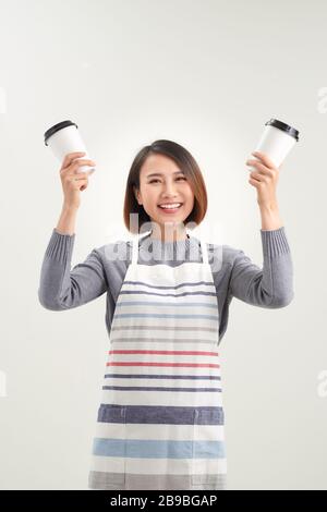 La ragazza affascinante tiene una tazza usa e getta con bevande e guarda direttamente alla macchina fotografica isolata su sfondo bianco Foto Stock