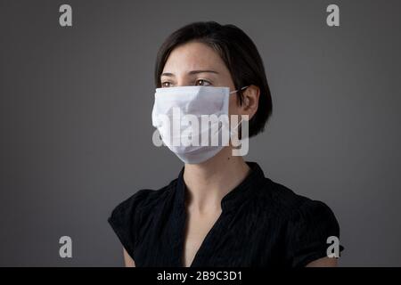 Donna brunetta che indossa la maschera igienica per prevenire le infezioni, malattie respiratorie trasmesse dall'aria come l'influenza, 2019-nCoV su sfondo grigio. Concetto di assistenza sanitaria. Foto Stock