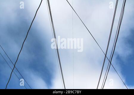 Intreccio di fili e cavi contro il cielo blu con nuvole. Paesaggio urbano industriale. Foto Stock