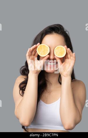 Ragazza dai capelli scuri che chiude gli occhi con l'arancio e sorridente Foto Stock