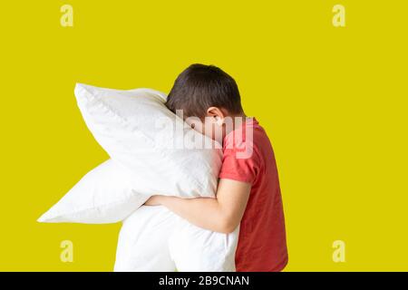 un ragazzo con due cuscini, senza maniche, concetto di sonno per bambini, sfondo giallo Foto Stock