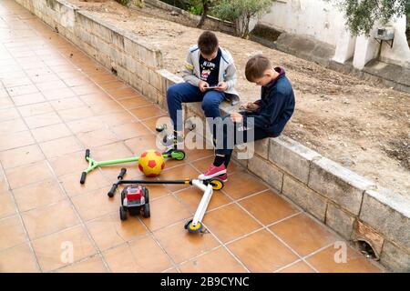 Il telefono cellulare è un problema moderno per i bambini. I bambini giocano al telefono nel parco. Giocattoli e scooter sono abbandonati. Aggiunta di smartphone in Foto Stock