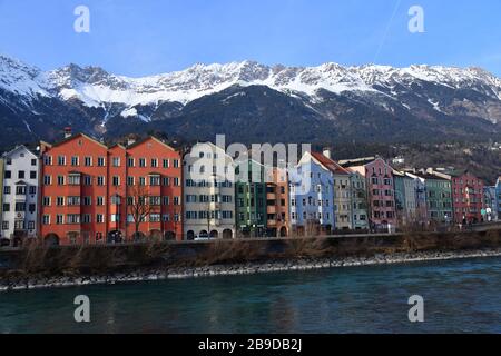 Fila di case colorate e luminose lungo il fiume la locanda di Innsbruck, Austria con maestose cime di montagna coperte di neve sullo sfondo Foto Stock