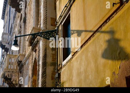 Luce di strada retrò a Venezia contro fisso su vecchio edificio che lancia un'ombra su parete gialla di casa adiacente Foto Stock