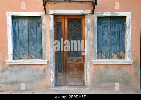 Chiudere la porta di ingresso e due finestre di casa sbiadita arancione e gialla a Burano Foto Stock