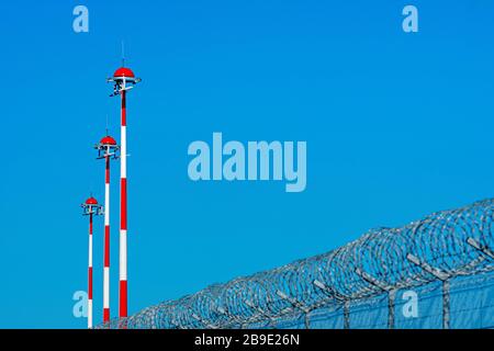 recinzione con filo spinato e fila di lampioni per l'aeroporto con pittura alternata rossa e bianca contro il cielo blu, concetto di sicurezza Foto Stock