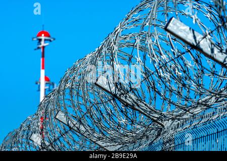 recinzione con filo spinato e fila di lampioni per l'aeroporto con pittura alternata rossa e bianca contro il cielo blu, concetto di sicurezza Foto Stock