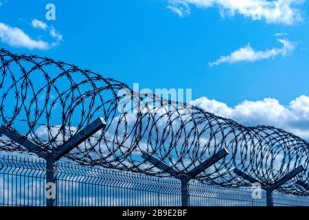 recinzione con filo spinato contro il cielo blu con nuvole, concetto di sicurezza Foto Stock