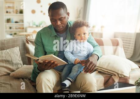 Ritratto di uomo maturo afro-americano lettura libro a bambino seduto sul giro dei padri, copia spazio Foto Stock