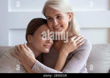 Sorridente madre più anziana abbracciando calma figlia adulta, godendo momento tenero Foto Stock