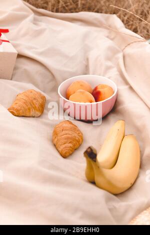 Pranzo al sacco con croissant, banana, frutta e una bottiglia di bevanda rossa all'aperto nel campo in una giornata di sole Foto Stock