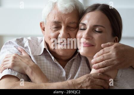 Felice figlia adulta e padre più anziano che abbracciano con occhi chiusi Foto Stock