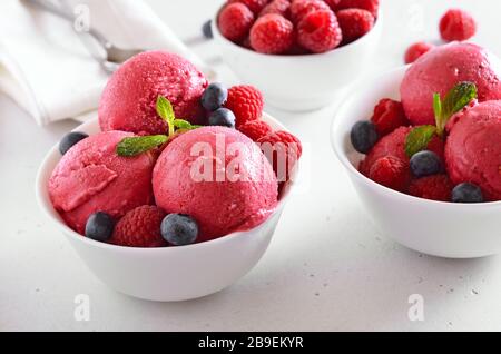 Gelato al lampone con lamponi freschi e mirtilli in ciotola su sfondo di pietra. Dessert estivo freddo. Foto Stock